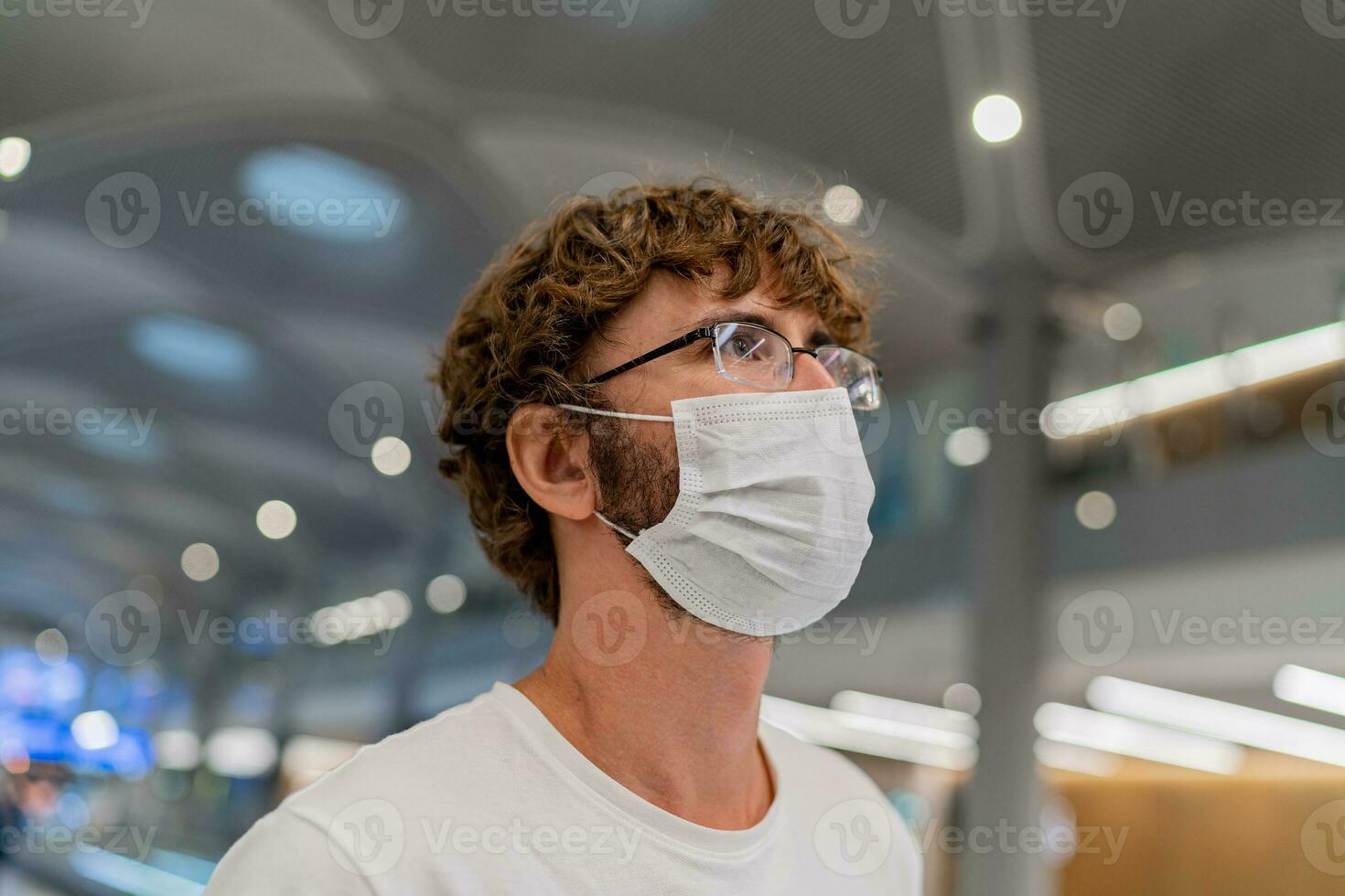 Traveler  man wearing face mask waiting to board info airplane, standing in departure terminal in airport. photo