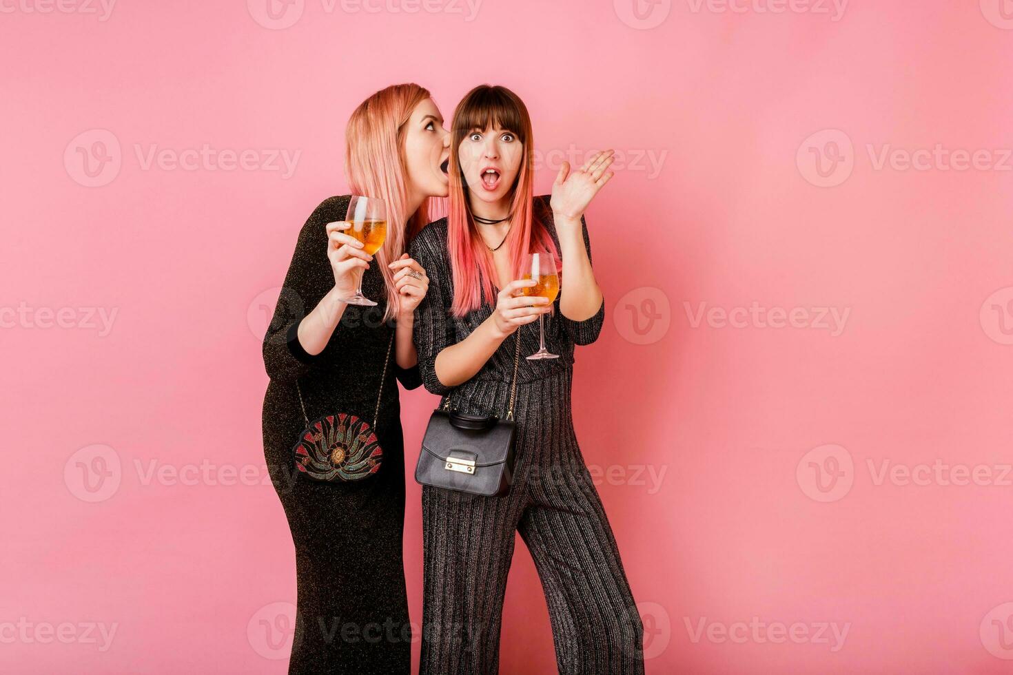 chisme muchachas con lentes de alcohol bebidas posando en ligero rosado antecedentes. fiesta humor. vistiendo lujo lentejuelas vestir . foto