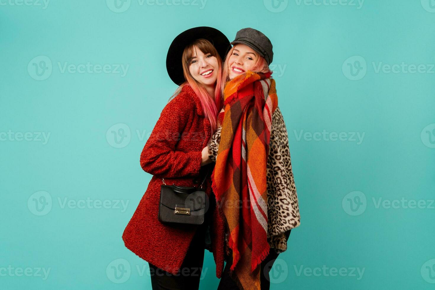Two stylish blond  women posing in studio on blue turquoise background. Friends hugging and having fun together.  Wearing leopard print faux fur coat and wool scarf. Winter fashion. photo