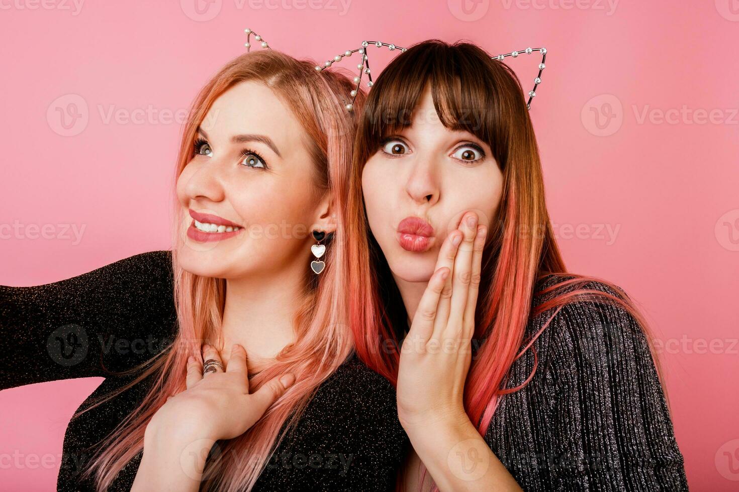 dos hermosa mujer en mascarada gato orejas haciendo yo retrato en rosado antecedentes. cerca arriba retrato de abrazando muchachas con sincero sonrisa. fiesta humor. foto