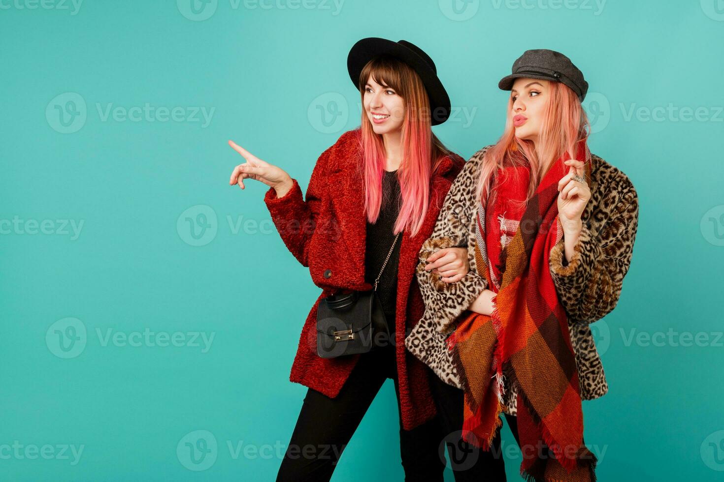 Fashionable studio shot of two stylish  models in bright winter or autumn   outfit, hat and scarf posing in turquoise  background. photo
