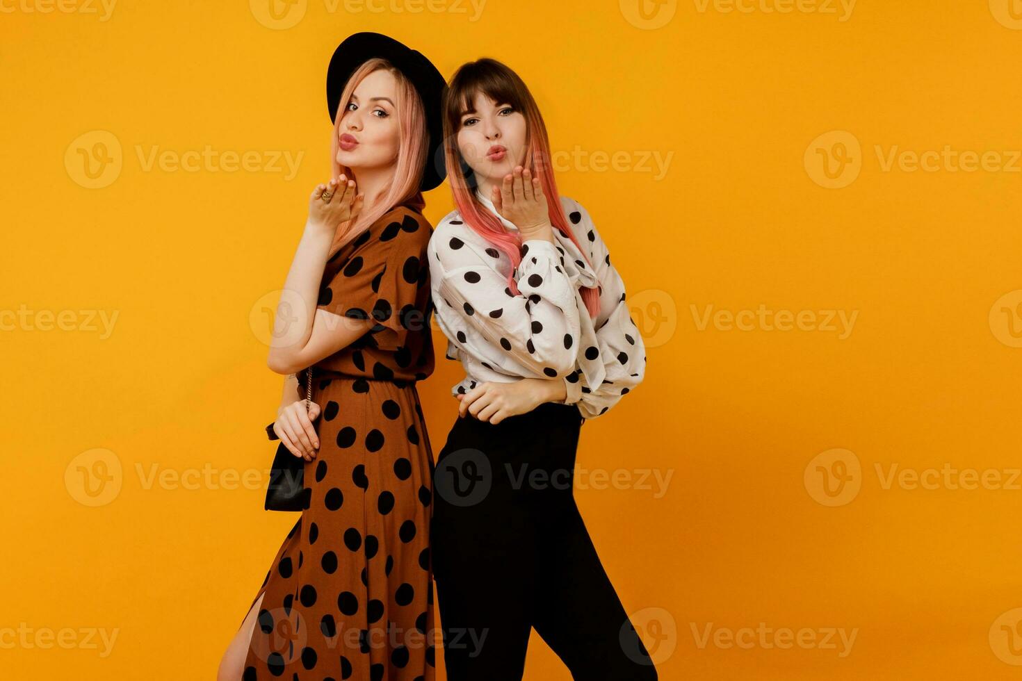 Couple of  lovely  women, fashionable friends sends kiss to camera and  posing over yellow background. Summer trendy vintage outfit. Shopping and fashion concept. photo