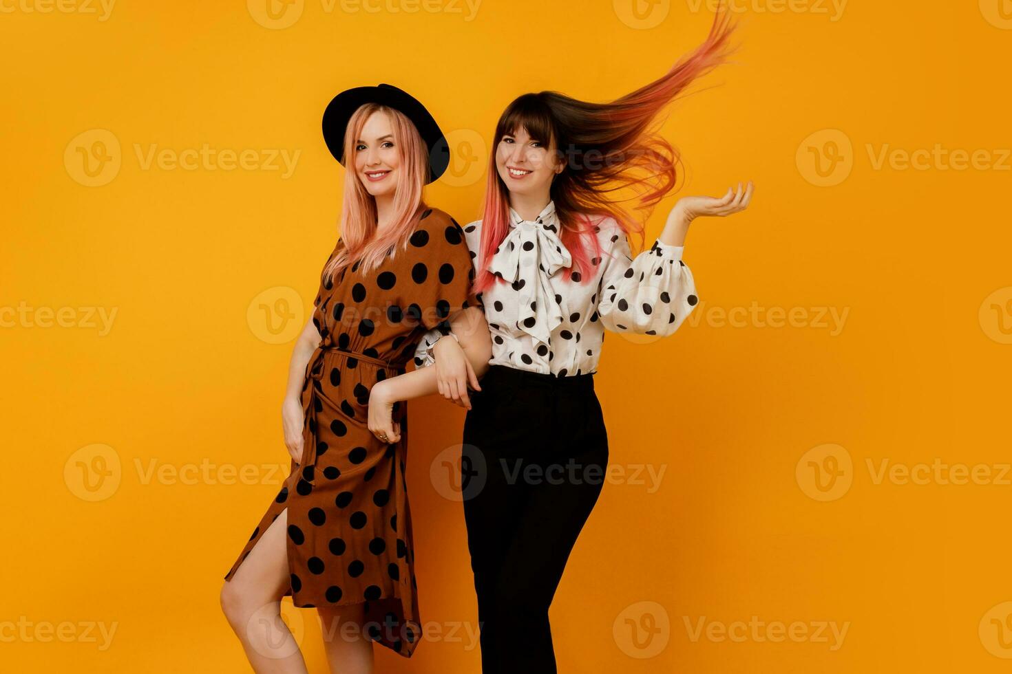 Image  of stylish elegant   females  in  dress   posing over  yellow background. Glad female models in stylish clothes. Trendy hat and bag. photo