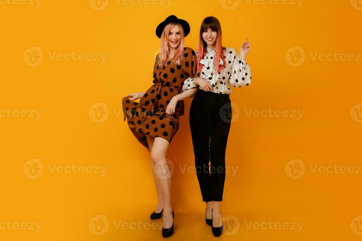 Full-length image  of stylish elegant   females  in  dress   posing over  yellow background. Glad female models in stylish clothes. Trendy hat and bag. photo