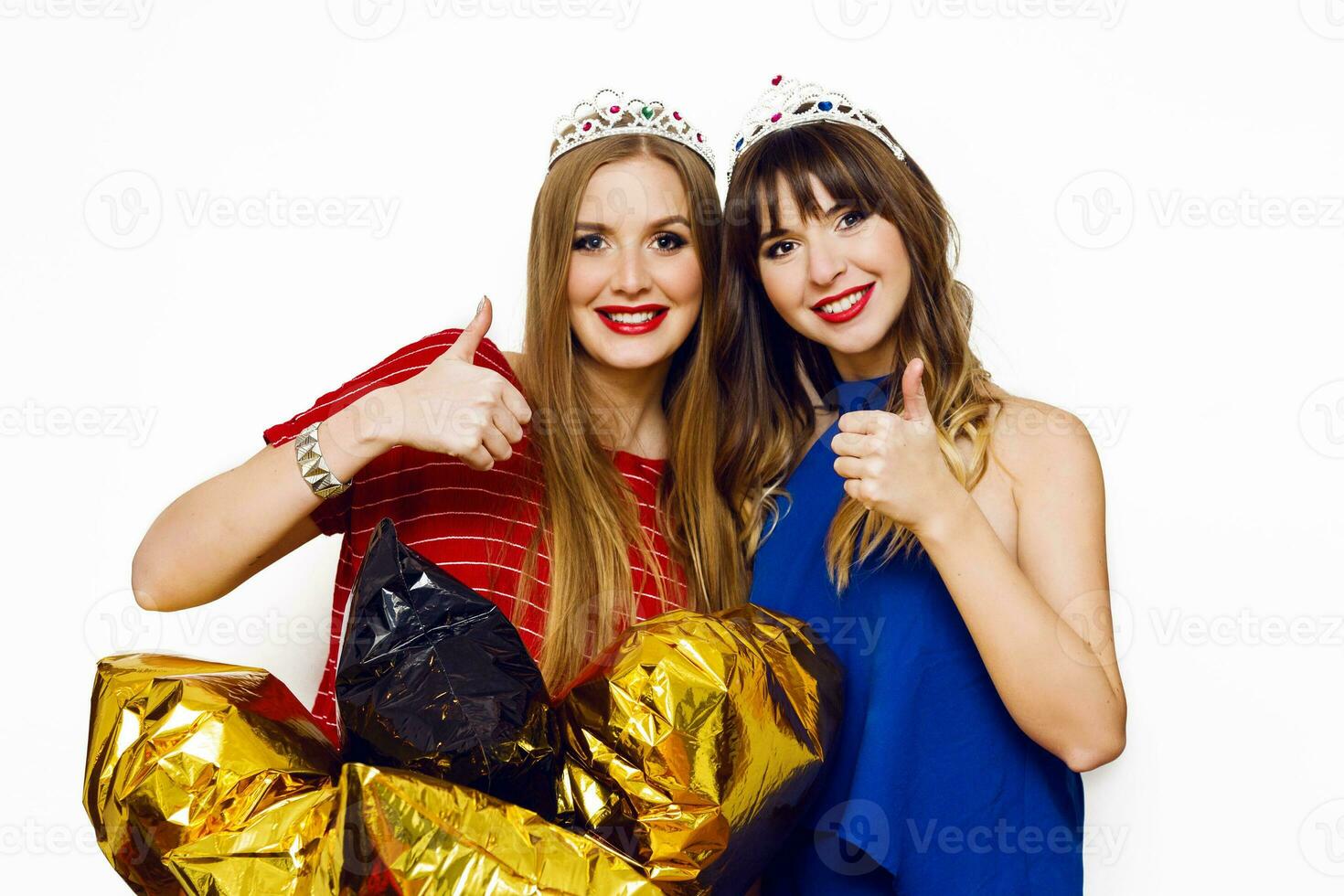 interior estilo de vida positivo retrato de dos bonito mujer, mejor amigos con brillante fiesta globos, mascarada coronas posando en blanco antecedentes. foto