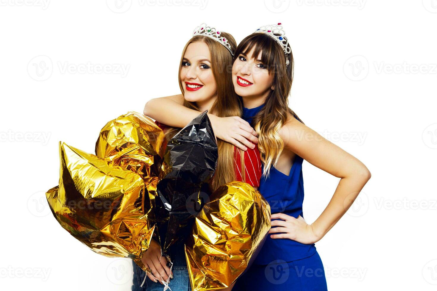 Indoor lifestyle positive portrait of two pretty women, best friends  with bright party balloons, masquerade crowns  posing  on white background. photo