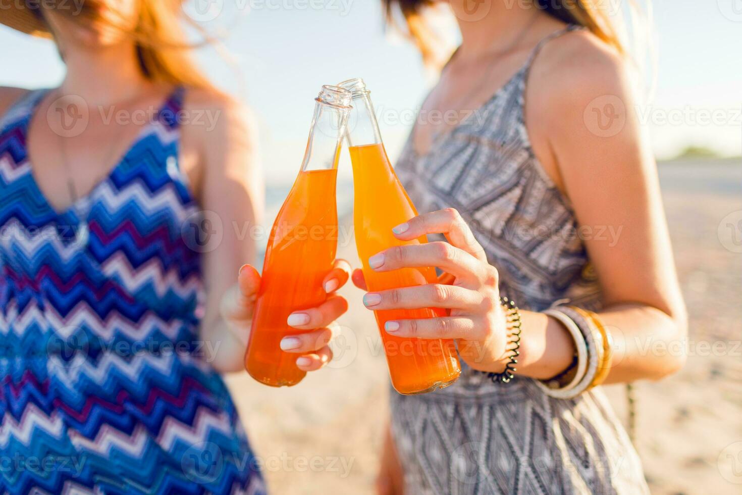 Summer holidays and vacation concept.  Friends drinking lemonade  or alcohol , holding beverage in bottles. Enjoying sunset on the beach. Party time. Focus on bottle. photo