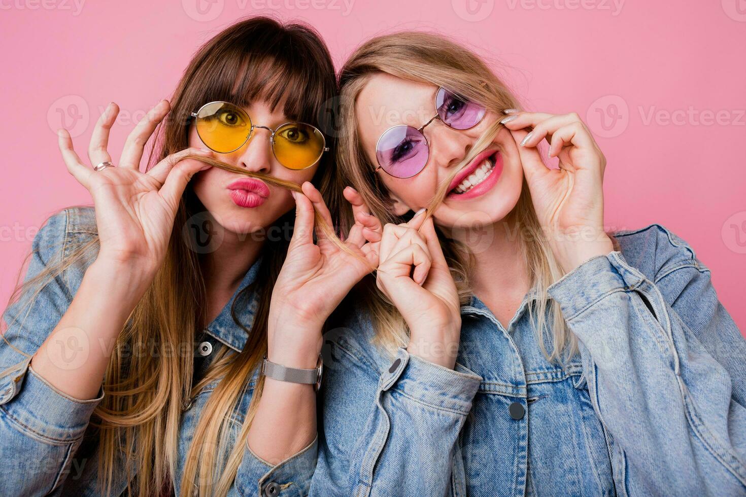 Lifestyle portrait of two  hipster girls best friends with bright make up , making funny faces and sending kiss over pink background. photo