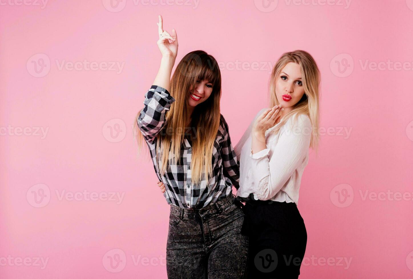 Two exited woman having fun and  raising hands up.  Standing on pink background.  Lucky  mood. photo