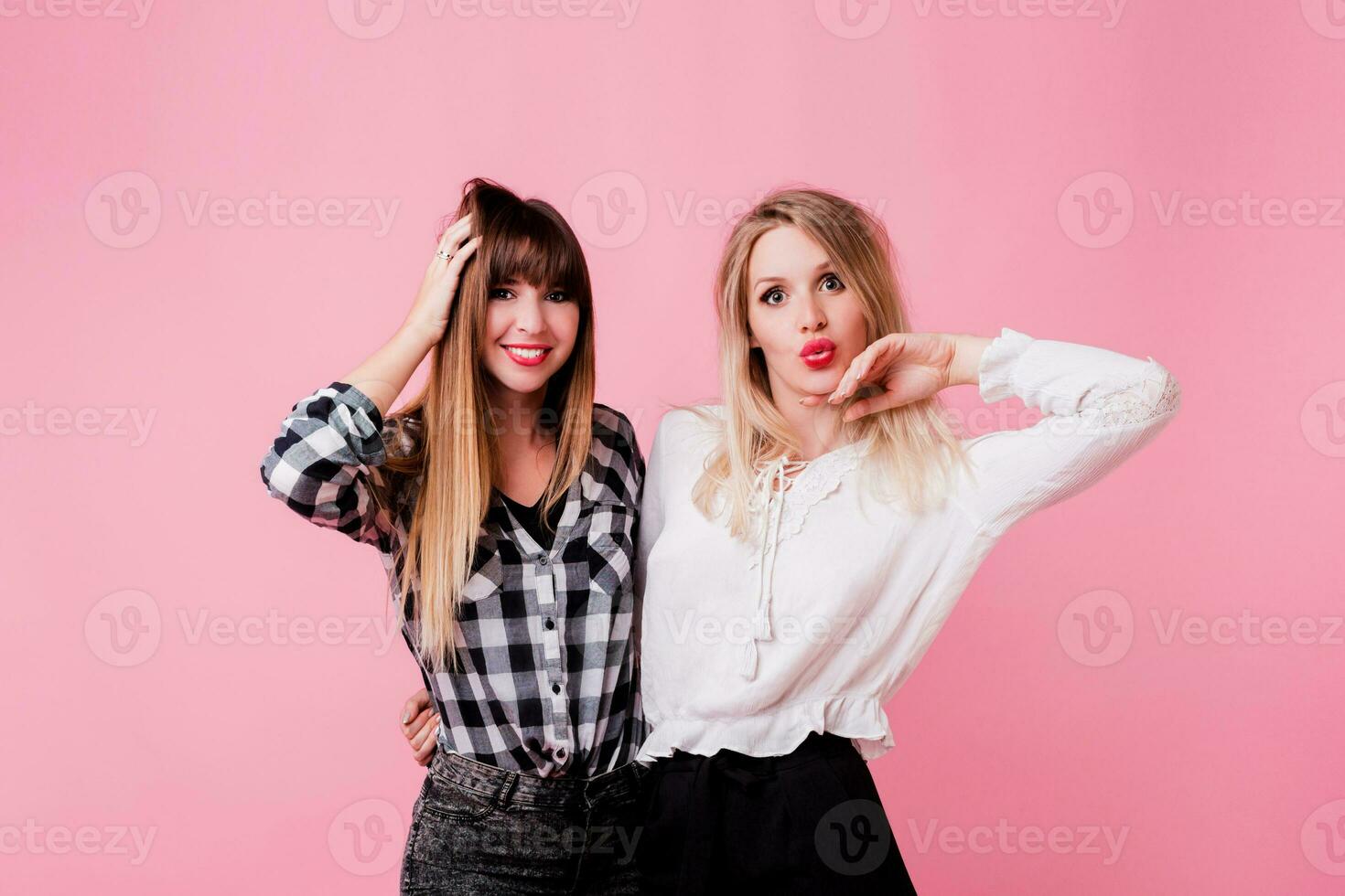 Two smiling women hugging and standing isolate over pink background . Brunette and blonde girls. Natural make up. photo