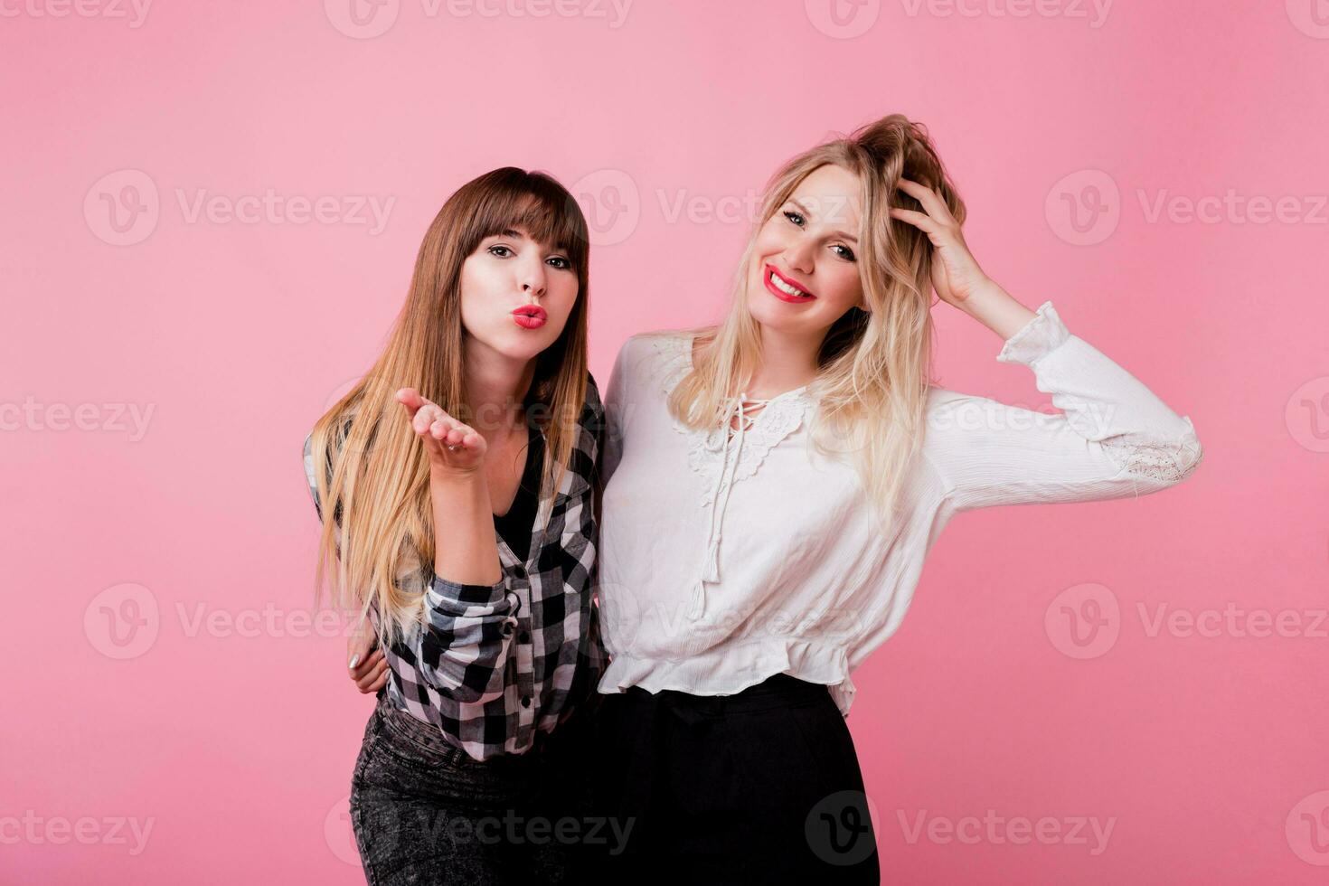 Two smiling women hugging and standing isolate over pink background . Brunette and blonde girls. Natural make up. photo