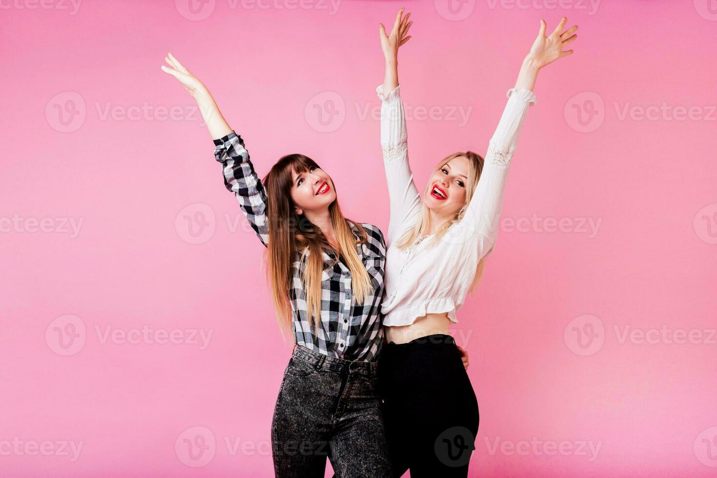 Two exited woman having fun and  raising hands up.  Standing on pink background.  Lucky  mood. photo