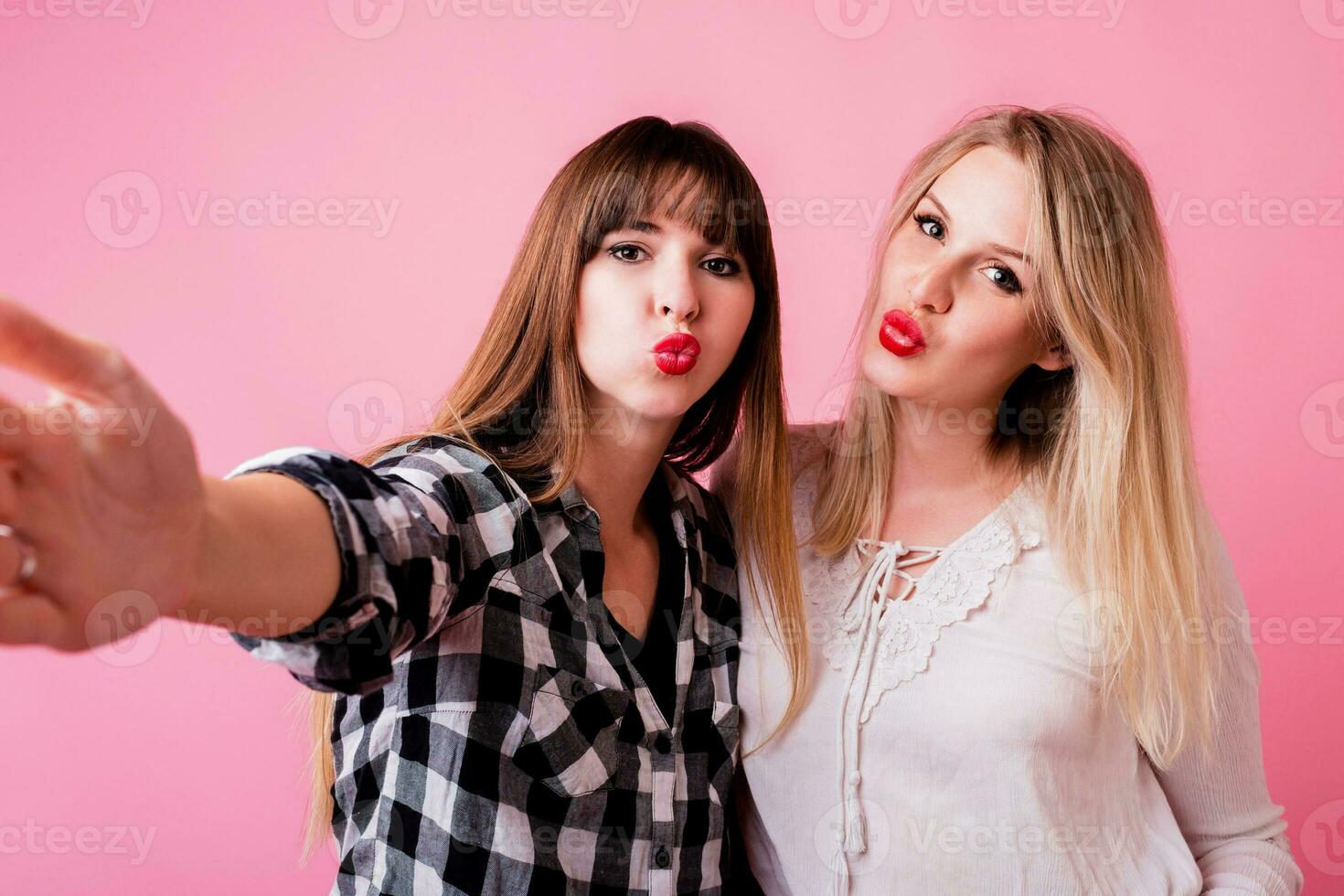 Two funny women making self portrait on pink background. photo