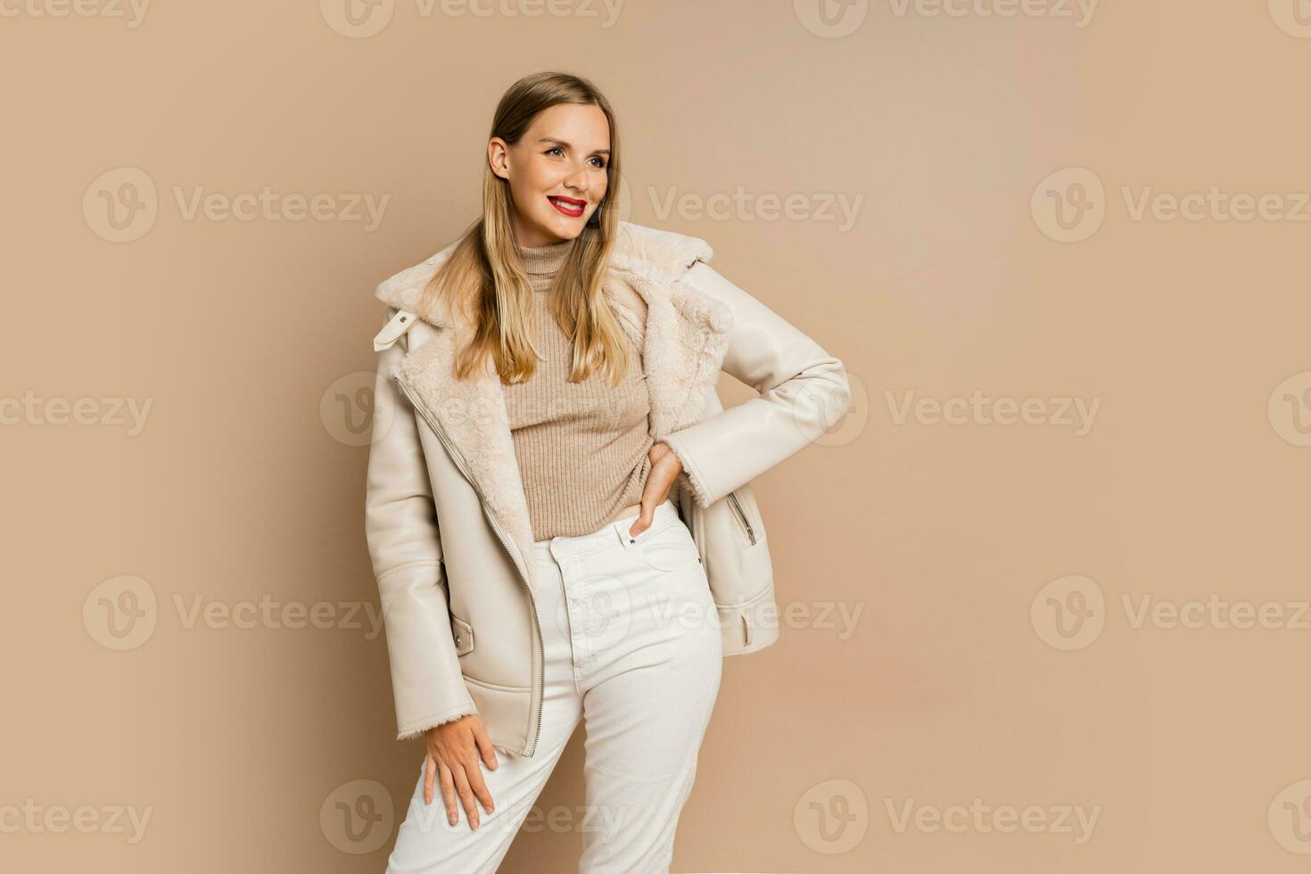 Pretty legant blond woman with red lips wearing trendy eco leather jacket , posing over beige background.  Winter fashion trends. photo