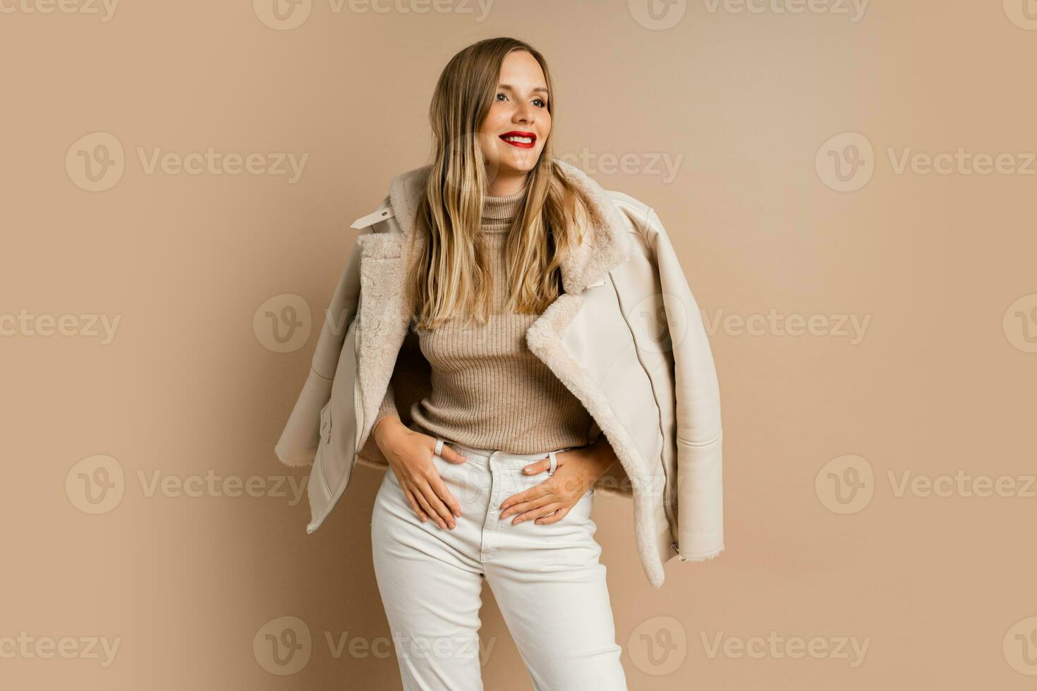Pretty legant blond woman with red lips wearing trendy eco leather jacket , posing over beige background.  Winter fashion trends. photo