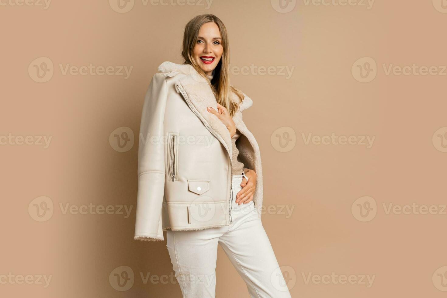 Pretty legant blond woman with red lips wearing trendy eco leather jacket , posing over beige background.  Winter fashion trends. photo