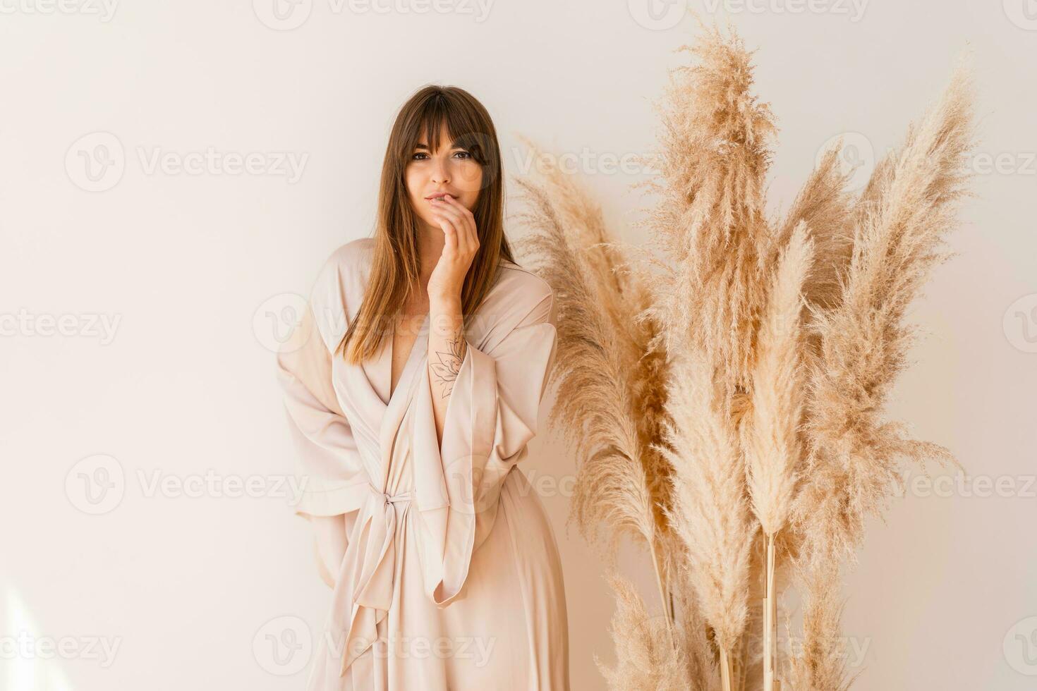 Elegant woman in stylish bohemian silk kimono posing over white background in studio with pampas grass decor. photo