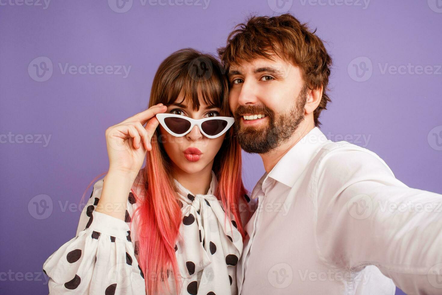 Pretty woman with candid smile and pink hairs posing with her boyfriend with beard. Hipster couple in love on purple background. Vintage sunglasses. photo