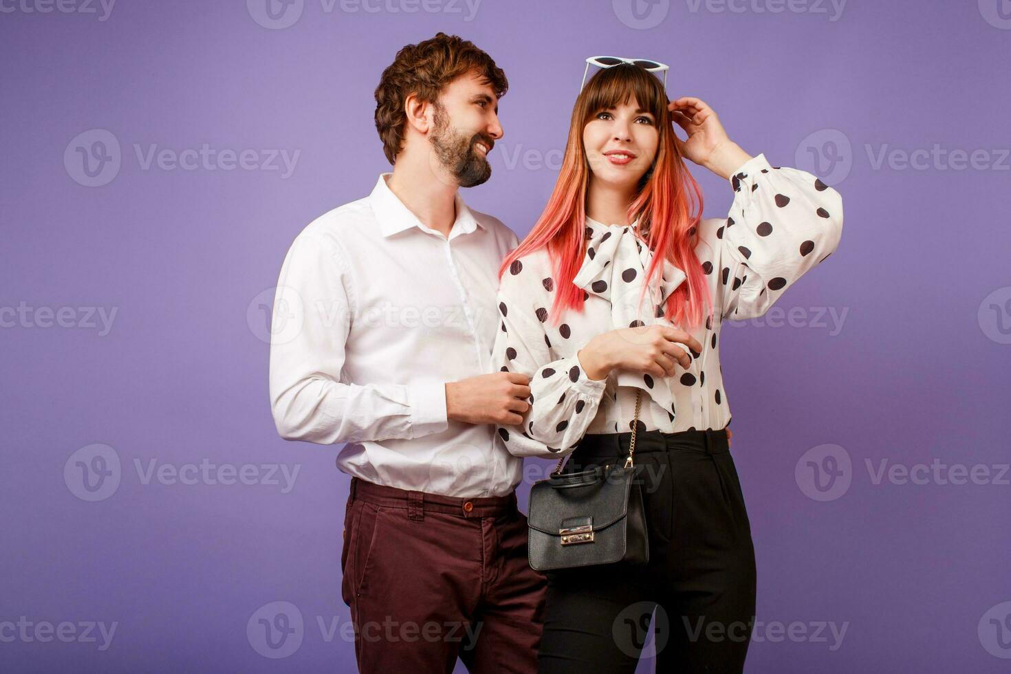 Cute couple hugging and looking on each other.  Handsome  man with beard and his pretty woman with pink hairs in stylish retro outfit posing on purple background in studio. photo