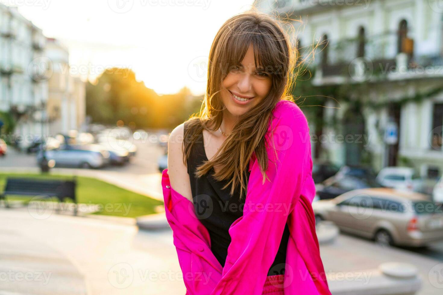 Outdoor summer portrait of debonair good loking woman in stylish pink shity. European street on background. Warm sunset colors. photo