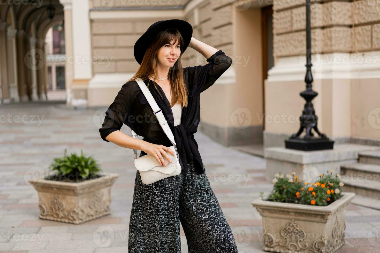 Street fashion photo of stylish brunette woman in casual outfit  and black hat. Enjoing vacation in european city.