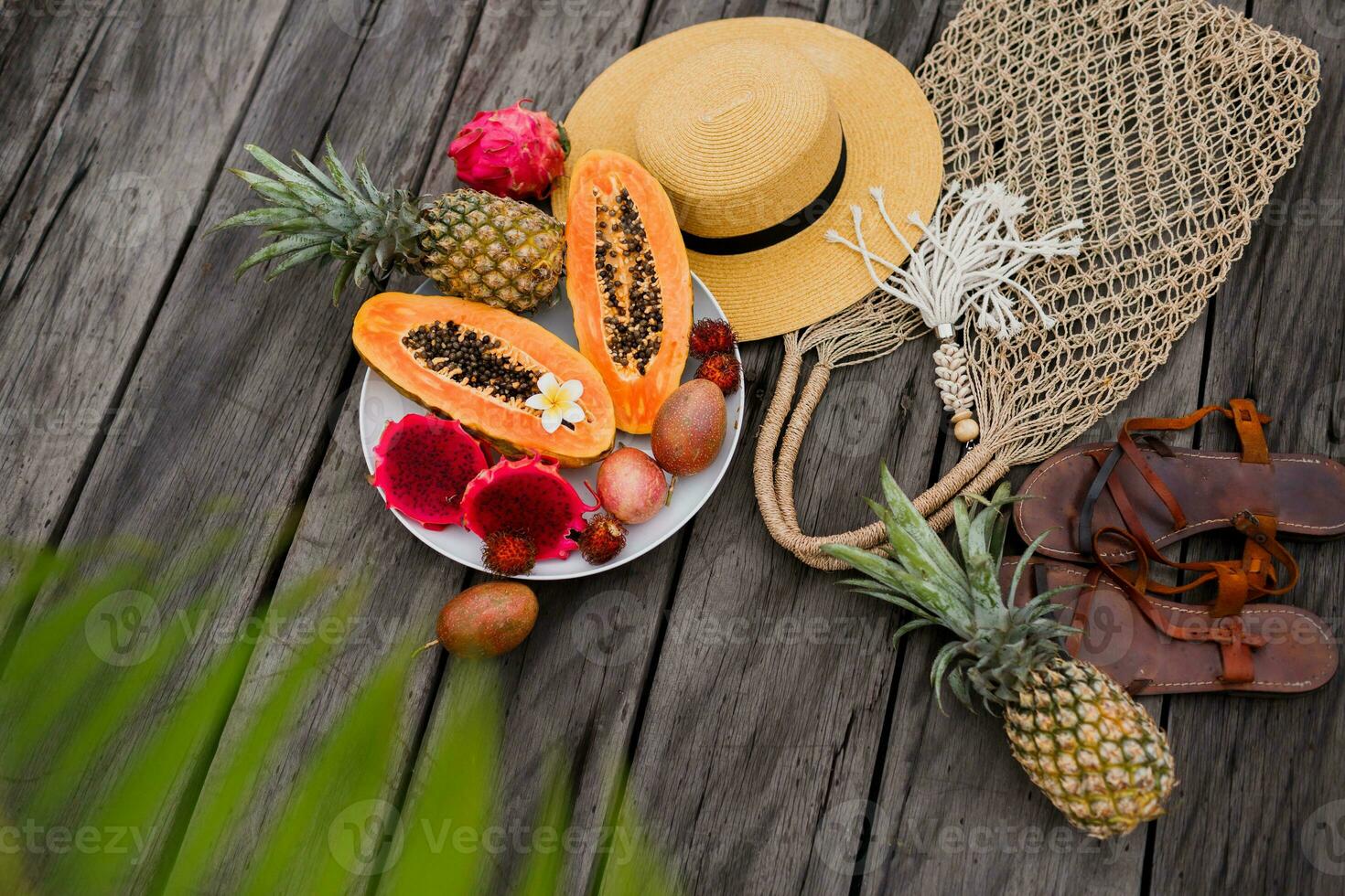 Summer tropical composition. Green palm leaves and tropical fruits on wood  background. Flat lay, top view. Straw hat and crochet woven bag. photo