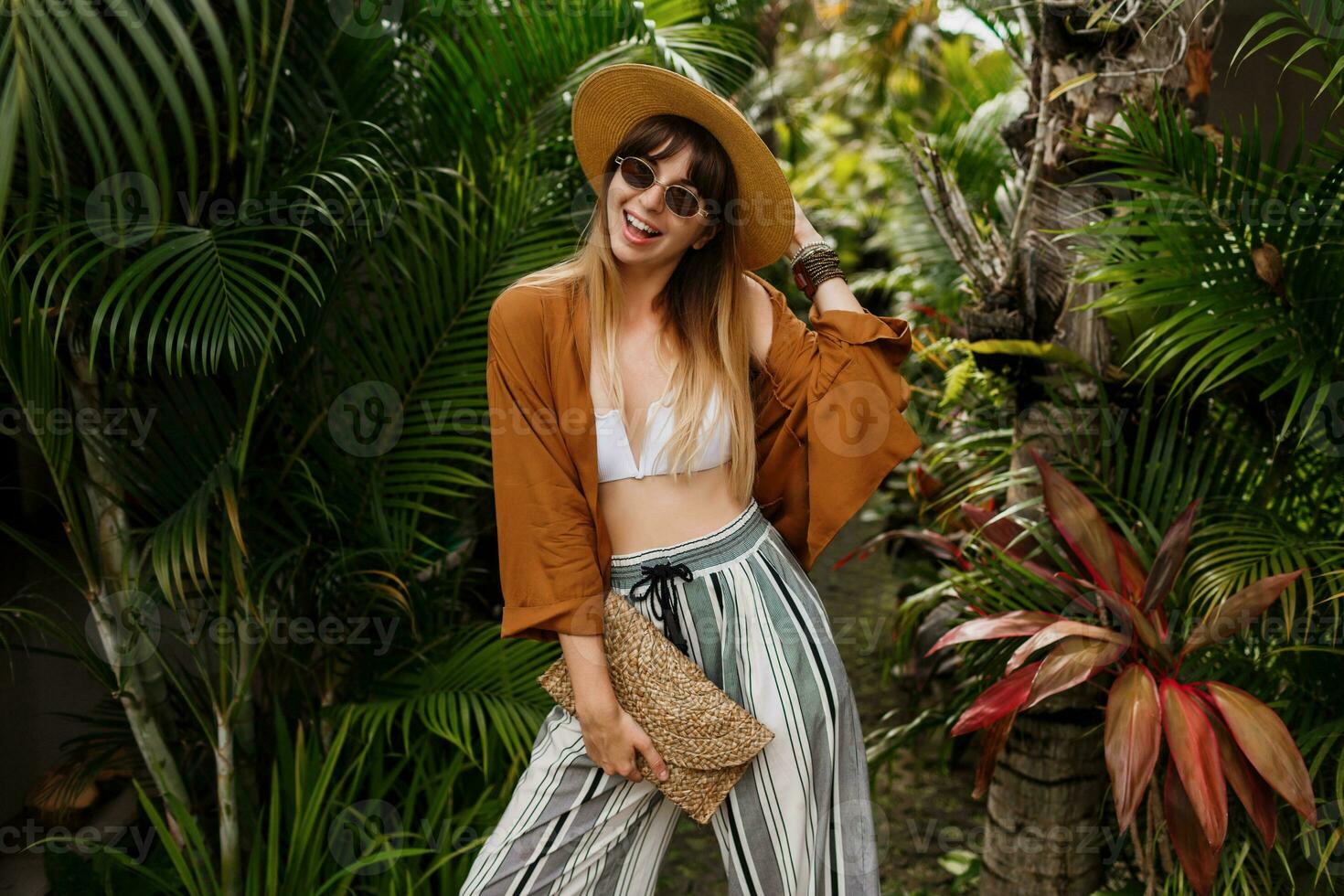 Fashion  image of  sexy graceful  woman in straw hat posing on tropical palm leaves background in Bali. Wearing stylish bohemian accessories. photo