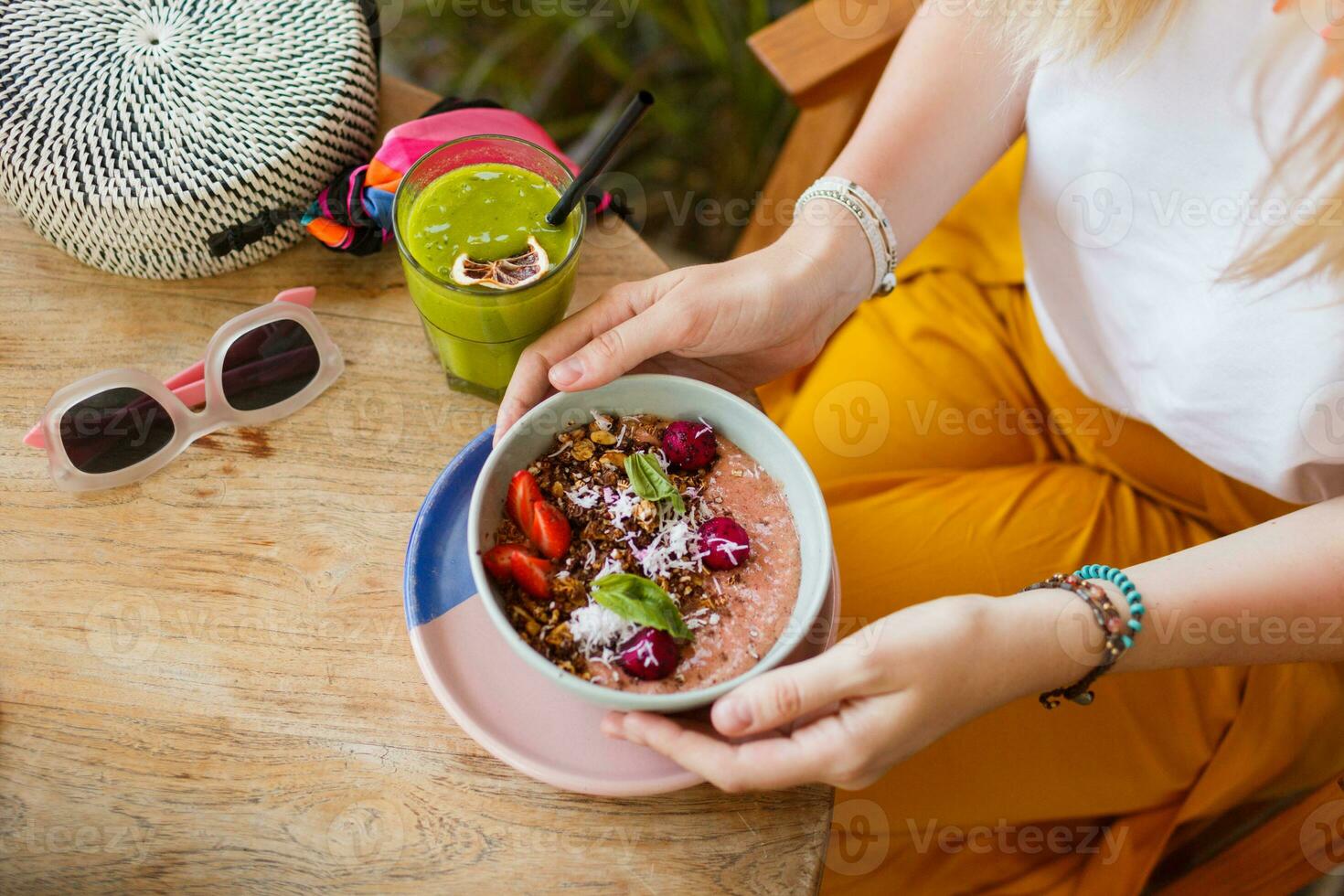 Woman holding smoothie. Superfoods  bowl topped with chia, granola and avocado. Overhead, top view, flat lay. Healthy breakfast. Summer accessories. photo