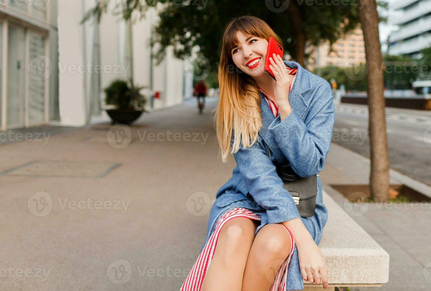 Successful smiling blond female talking by mobile phone on urban background after work. Sitting on bench. photo