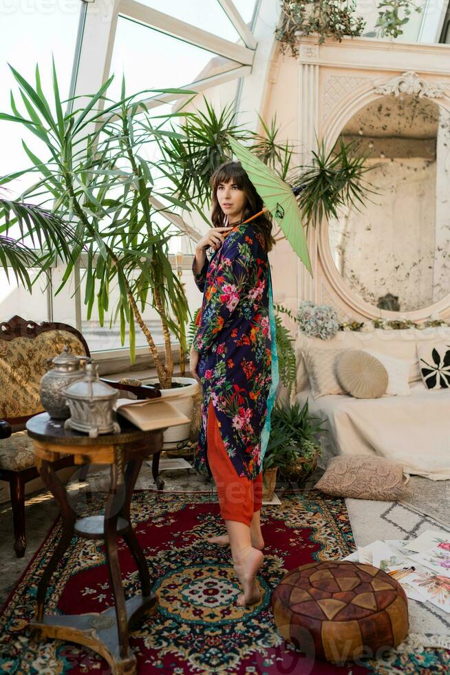 Woman with japanese umbrella popsing in  boho interior  with tropical plants and stylish furniture. photo
