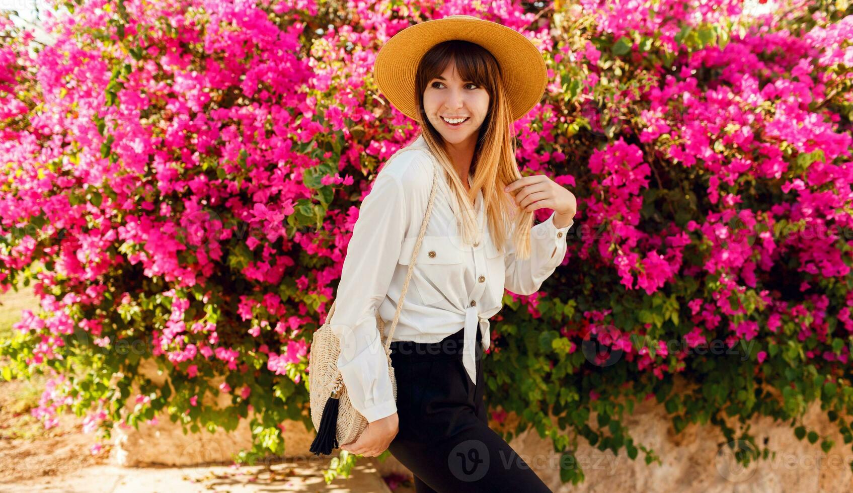 Good looking happy  woman standing over  flowers background. Wearing straw hat and casual outfit. photo