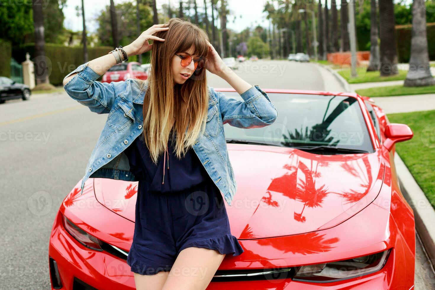 Lifestyle image of travel  female  sitting  on the hood of amazing red convertible  sport car. Streets of  Los Angeles on background. photo