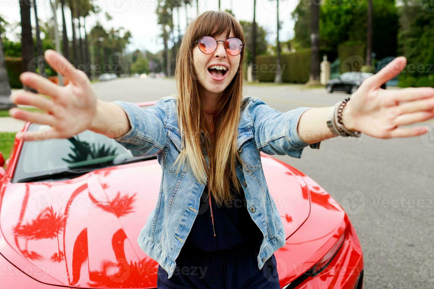 Cute   happy woman in pink glasses making self portrait near amazing red convertible  sport car in California. photo