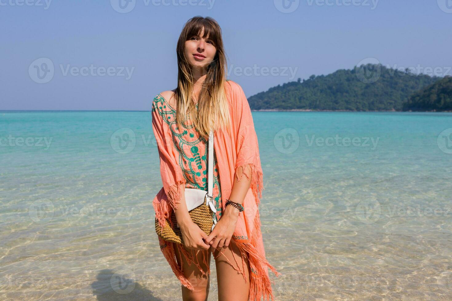 Outdoor summer portrait of stylish tan  pensive woman  in trendy boho beach dress with embroidery and tassel. Straw  bag. photo