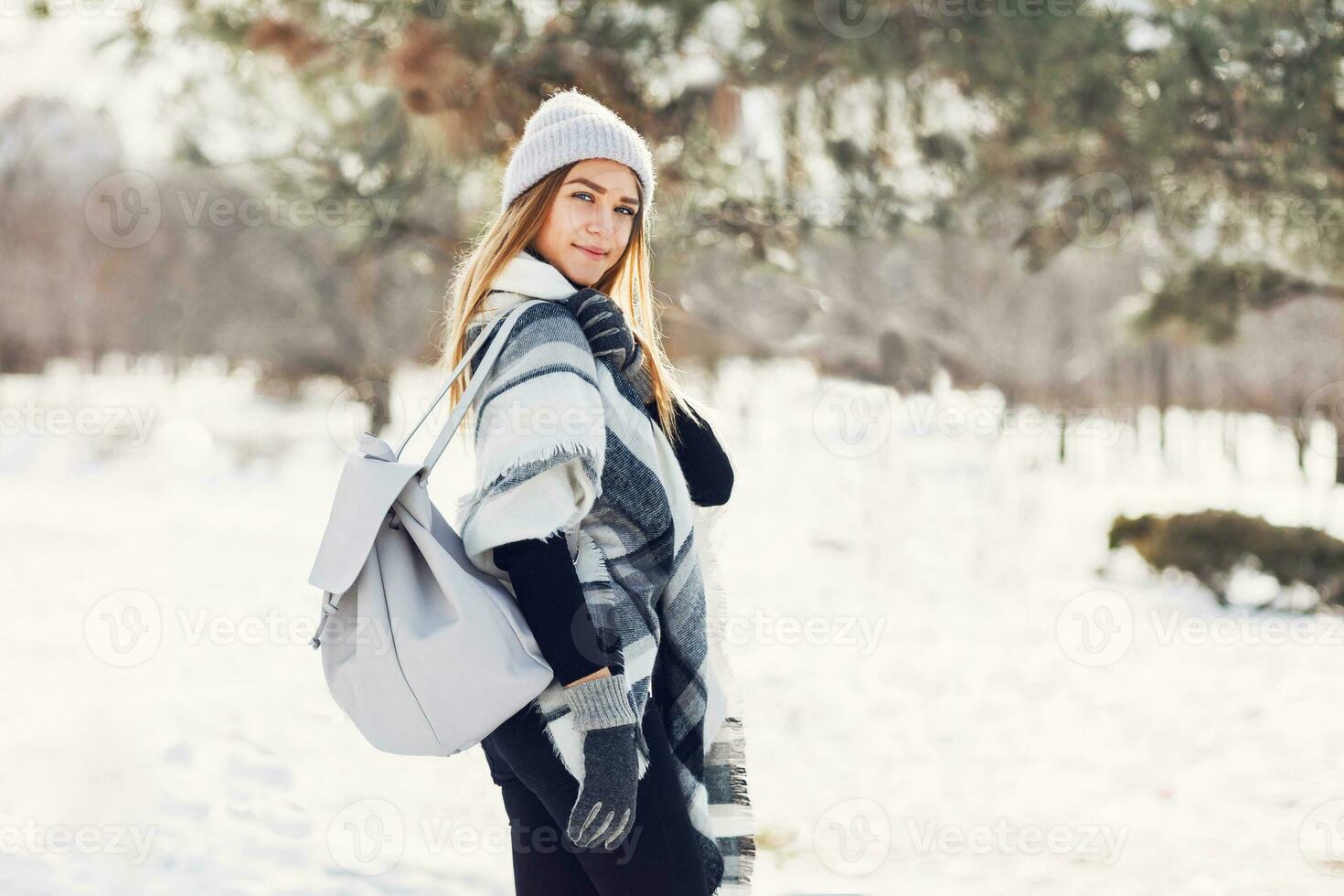 Winter lifestyle portrait of young blonde lady in warm wool  fluffy  scarf and  hat with backpack walking in wonderful winter park. photo