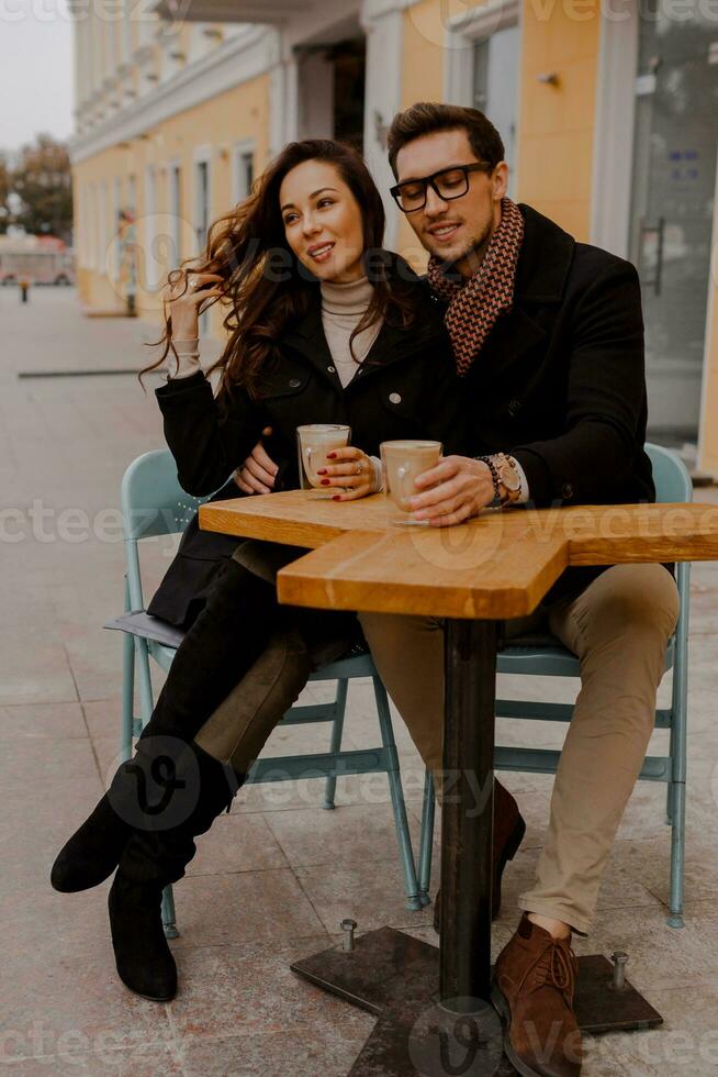 Fashionable couple in love sitting in street cafe  and drinking hot coffee while traveling in Europe. photo