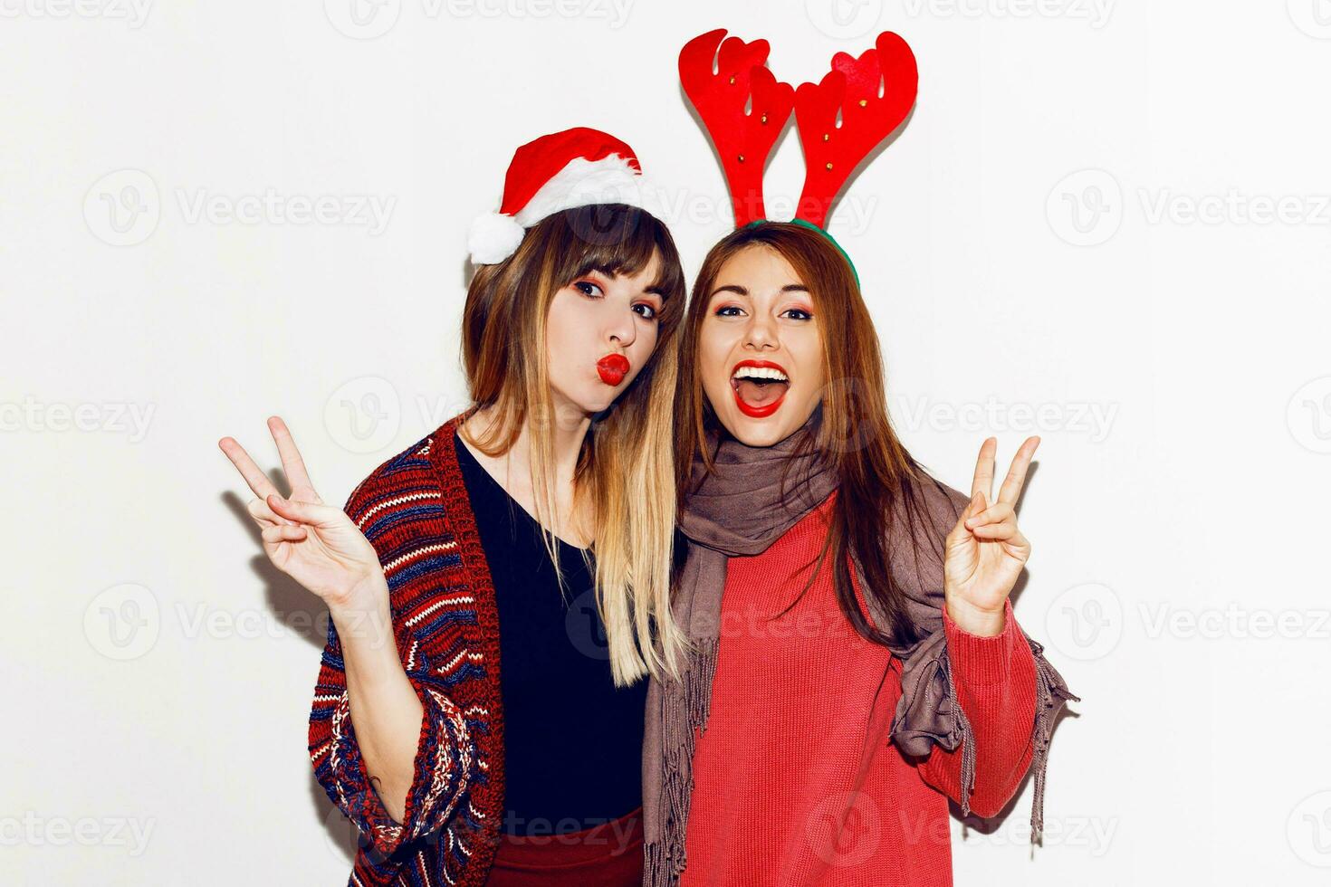 New year party. Two  beautiful girls  in funny masquerade Santa hats send kiss . Indoor stockpile image of best friends posing on white background. Isolate. photo