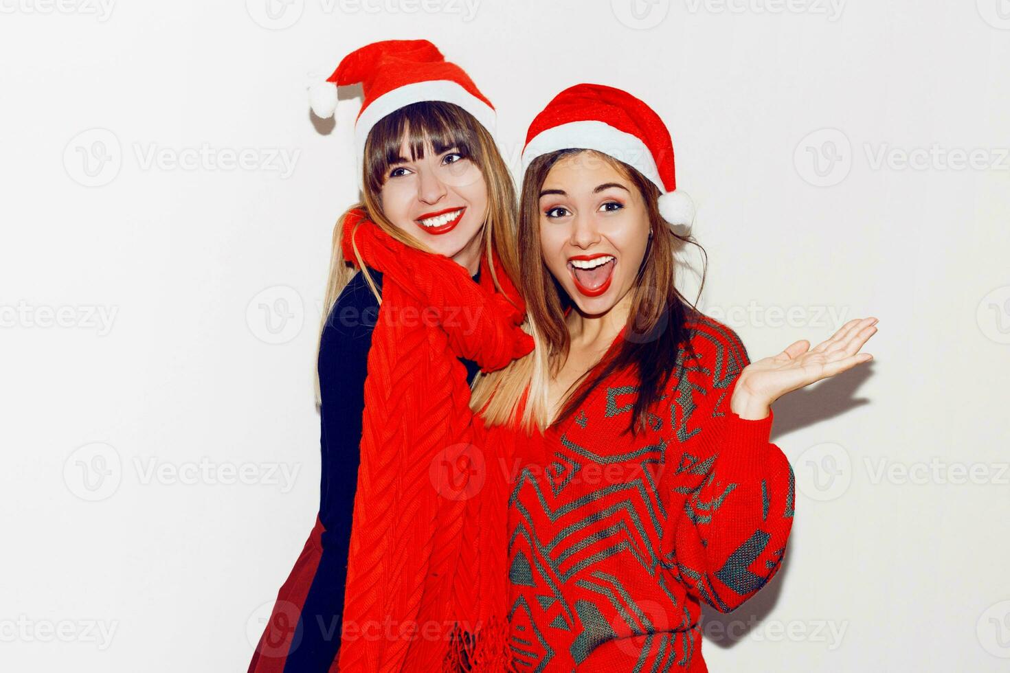 Crazy new year party mood. Two drunk laughing women having fun and posing on white background in cute masquerade hats. Red sweater and scarf. photo