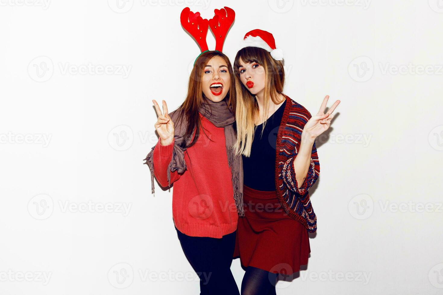 New year party. Two  beautiful girls  in funny masquerade Santa hats send kiss . Indoor stockpile image of best friends posing on white background. Isolate. photo