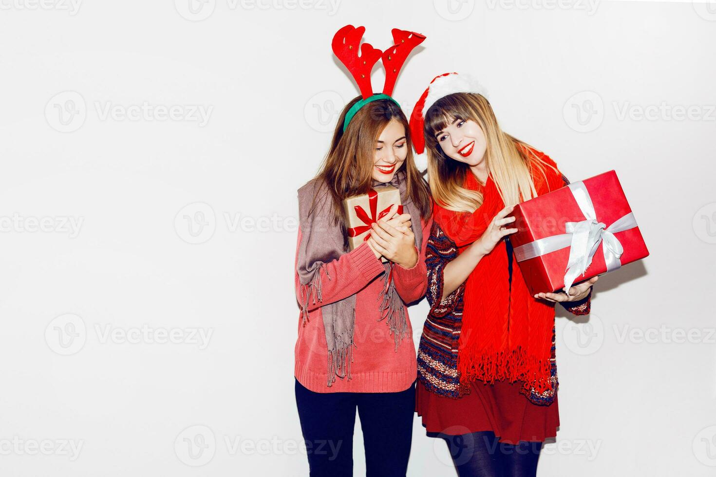 Two women  hid faces behind gifts on white background. Wearing cute masquerade hats. Celebrating mood. Flash portrait. photo
