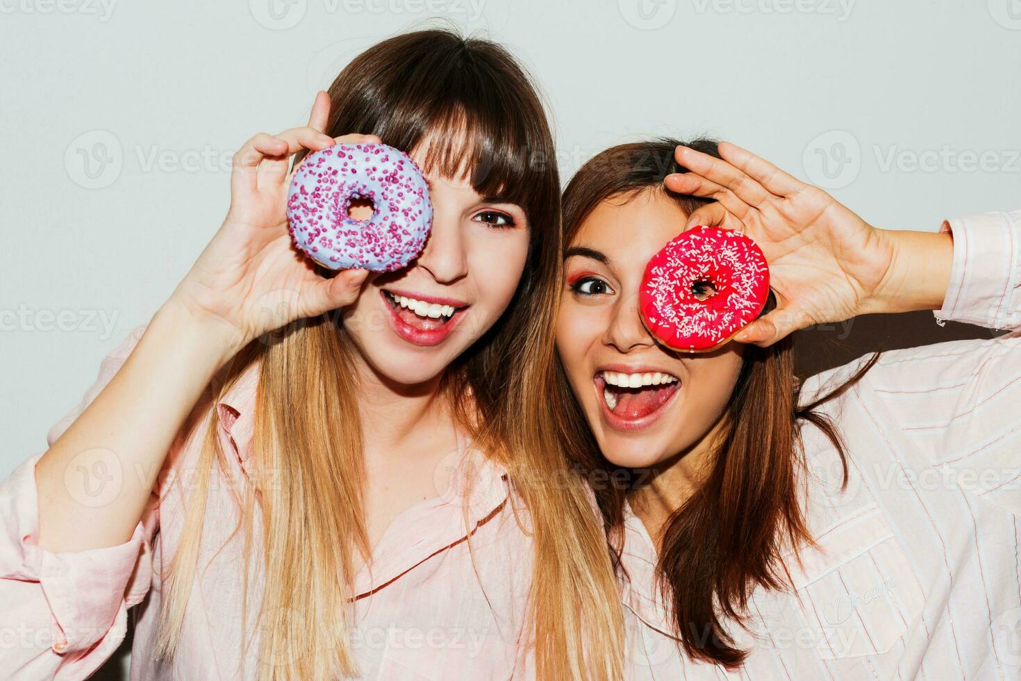 Home pajamas party.  Close up flash portrait of two funny  white women posing with donuts. Surprise face. photo