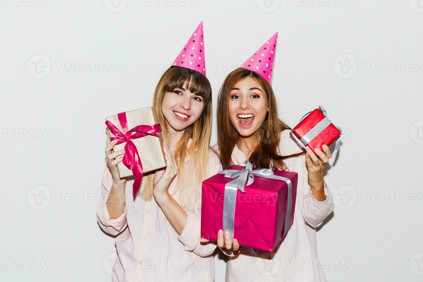 Pajamas  birthday party. Friends having fun and holding gift boxes. Surprise face, exited emotions. Girls wearing prop party hats. photo