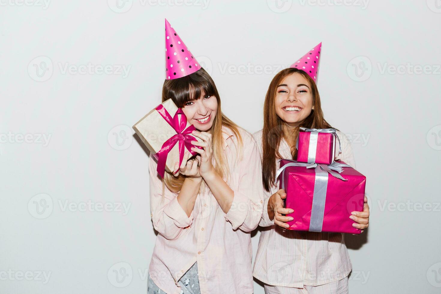 Pajamas  birthday party. Friends having fun and holding gift boxes. Surprise face, exited emotions. Girls wearing prop party hats.  Indoor. photo