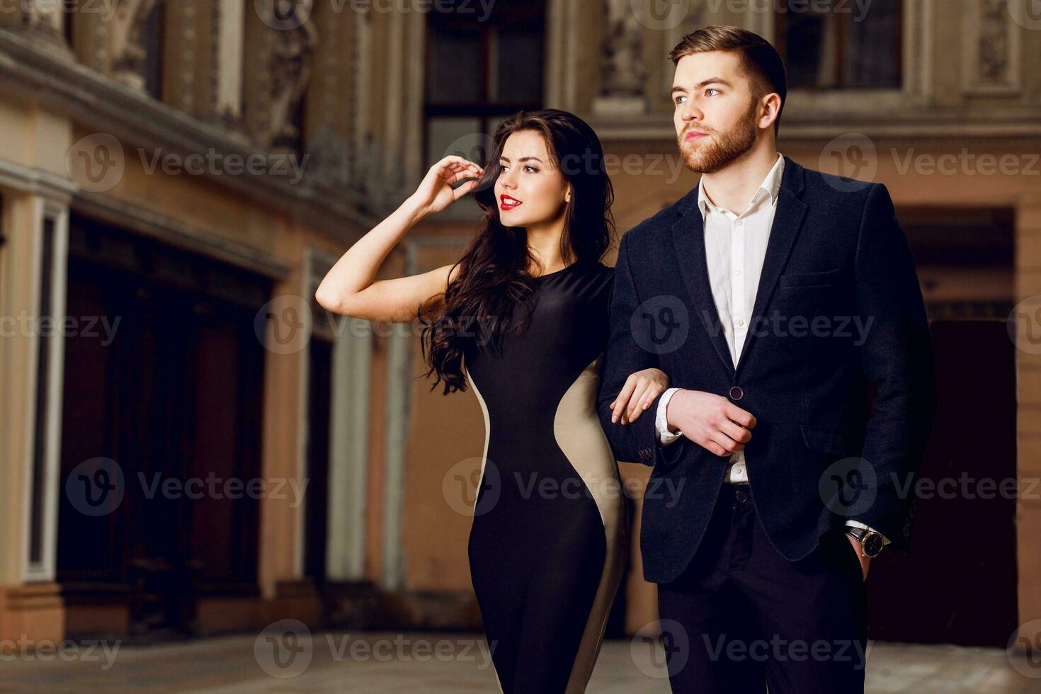 Couple in love in elegant outfit walking in old town street . Pretty brunette woman with red lips and her handsome boyfriend have time off in the evening. photo