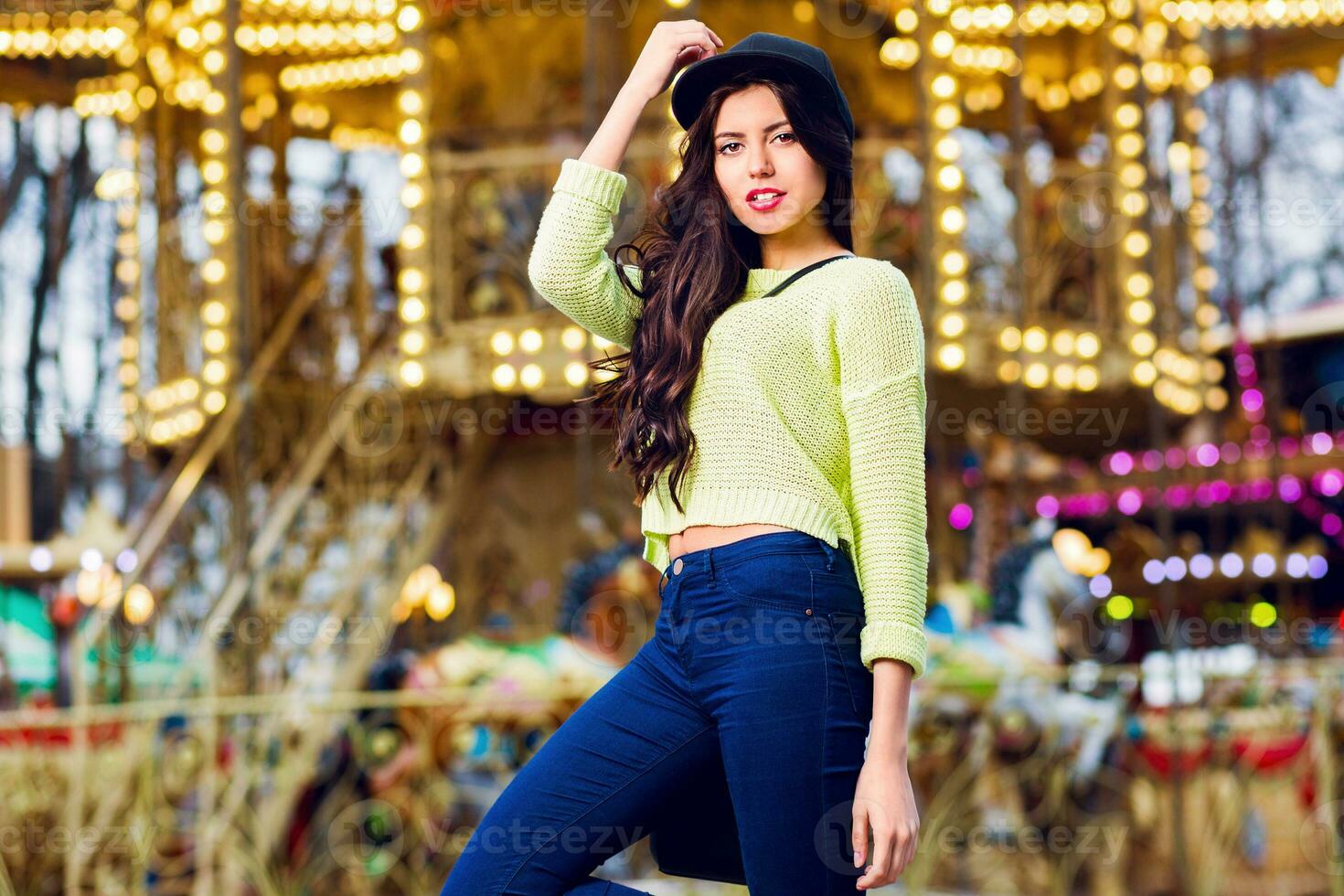 Close up portrait of sexy  stylish  girl  have fun and smile on attractions. Wearing trendy hipster swag  hat and neon sweater . Have perfect body and bright make up . photo