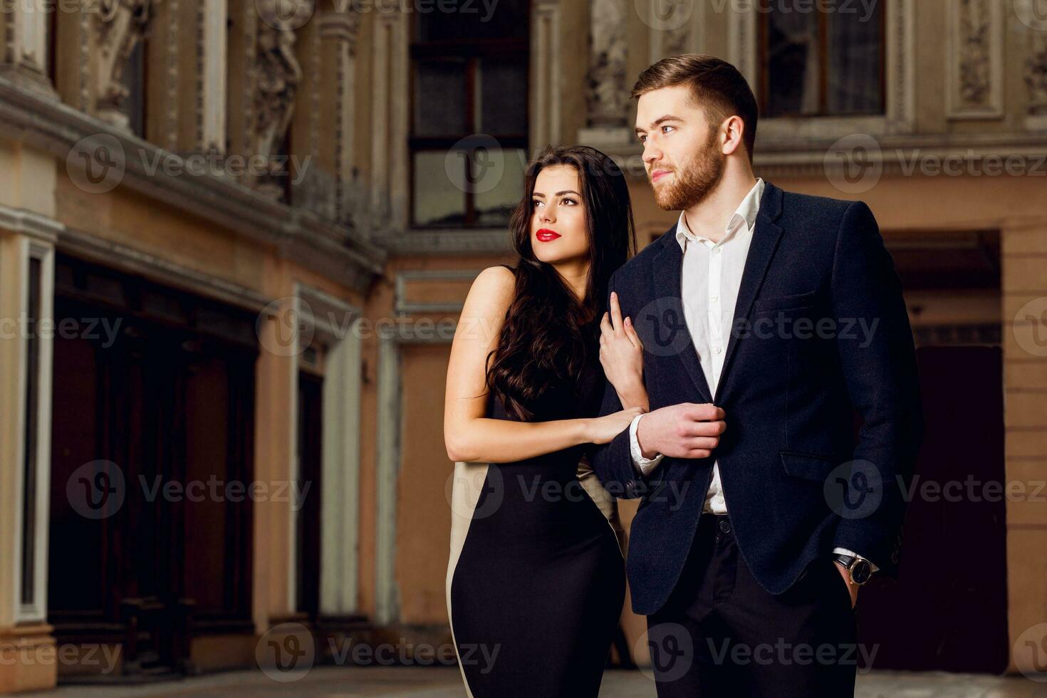 Couple in love in elegant outfit walking in old town street . Pretty brunette woman with red lips and her handsome boyfriend have time off in the evening. photo