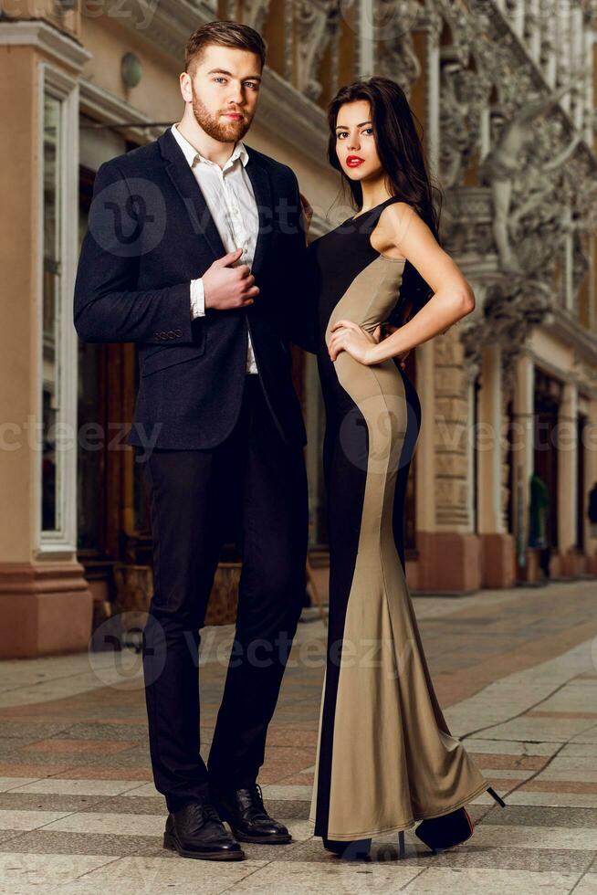 Couple in love in elegant outfit walking in old town street . Pretty brunette woman with red lips and her handsome boyfriend have time off in the evening. photo