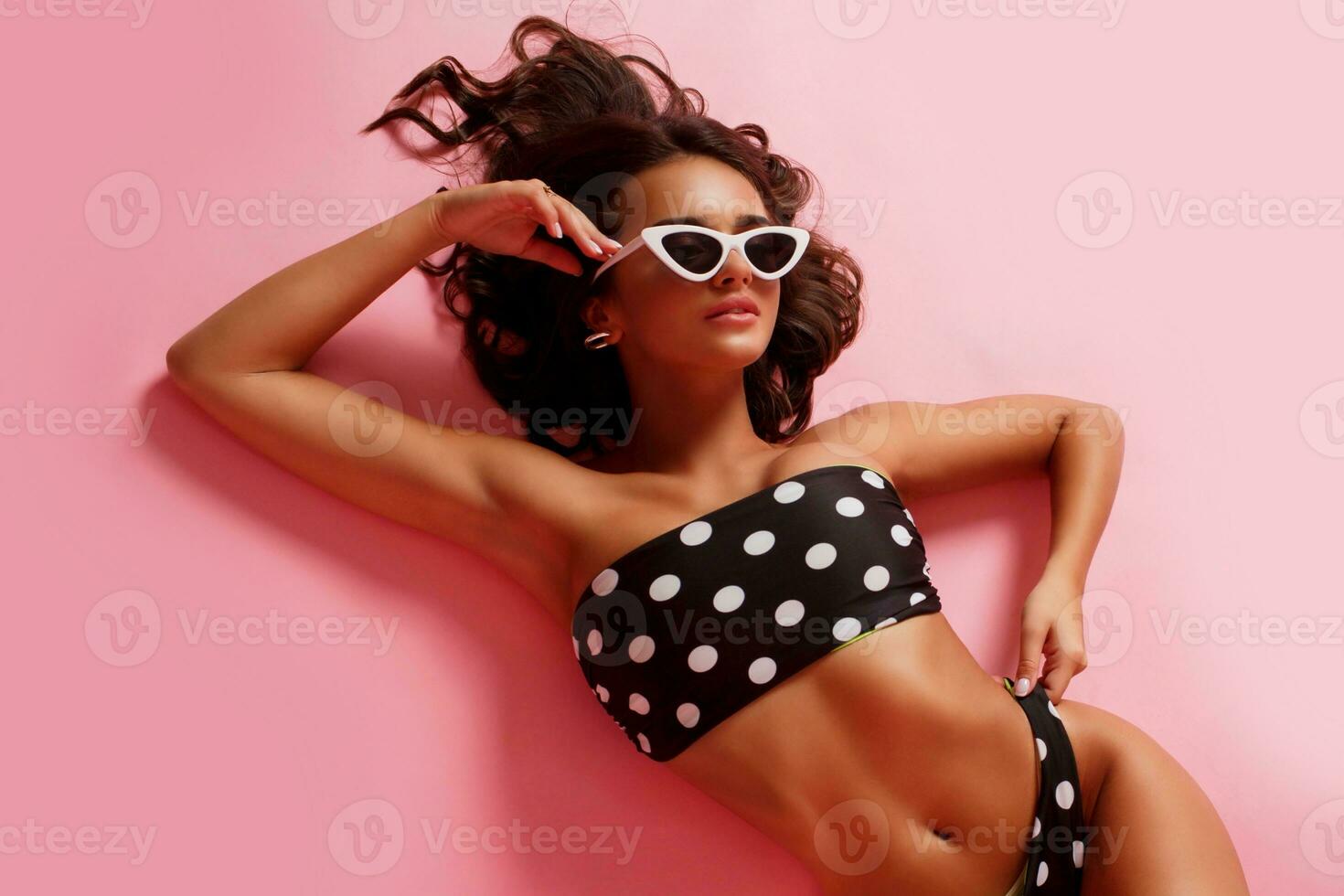 Top view of glamour sexy woman lying in swimwear on pink background. Studio photo. Perfect tan body. photo