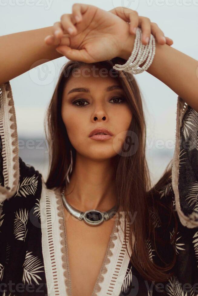 Close up portrait of  beautiful Asian woman in bohemian dress, ethnic jewelry and earring with feathers posing on the beach. photo