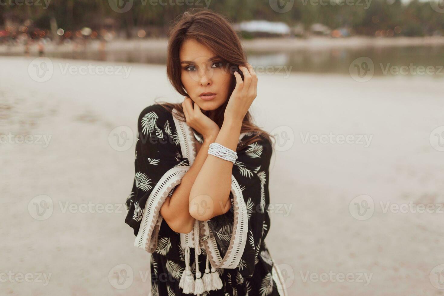 Beautiful Asian woman in tropical bohemian dress posing on the beach. Wearing earrings with feather, necklace and bracelets. photo